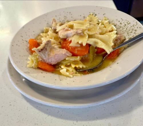 A bowl of pasta with carrots and pieces of meat, garnished with herbs, served on a white plate.