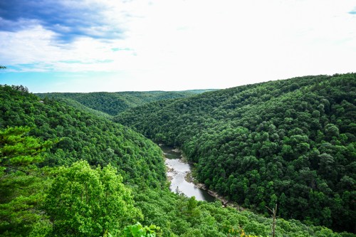 A scenic view of a winding river surrounded by lush green hills under a partly cloudy sky.
