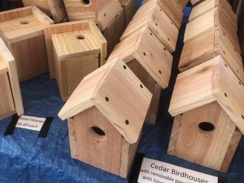 A display of wooden birdhouses with sloped roofs, some labeled as wren houses, on a blue tablecloth.