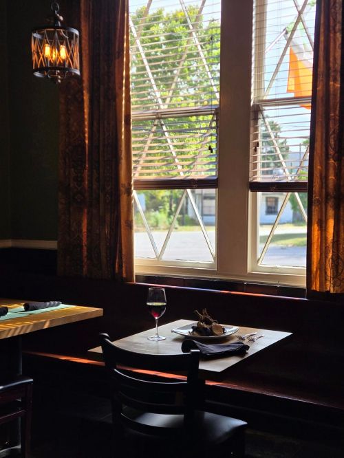 A cozy restaurant table set for dining, with a glass of red wine and sunlight streaming through the window.