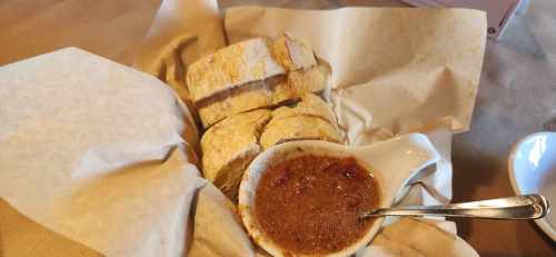 A basket of sliced bread with a small dish of brown dipping sauce on a table.