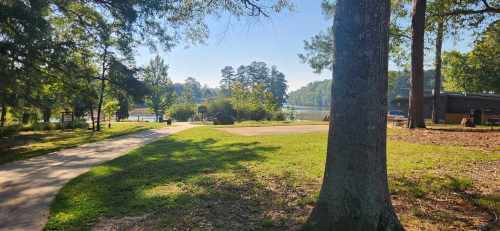 A serene lakeside view with a path, trees, and a clear blue sky, inviting outdoor relaxation.