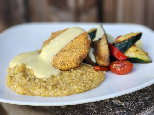 A plate featuring crispy fried chicken, creamy sauce, and a side of roasted vegetables and grain.