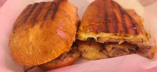 Two grilled sandwiches with crispy bread, filled with layers of meat and melted cheese, served in a paper wrapper.