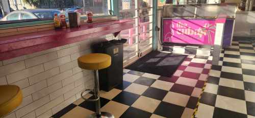 A colorful diner interior with a pink counter, yellow stools, and a checkered black-and-white floor.