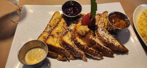 A plate of French toast topped with powdered sugar, served with fruit preserves and a strawberry garnish.