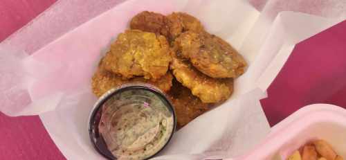A basket of golden fried plantain chips with a small cup of dipping sauce on the side.