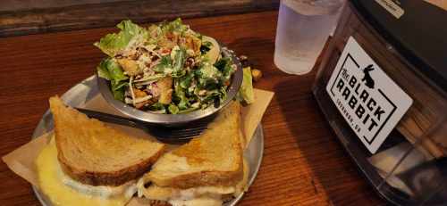 A plate with a grilled cheese sandwich and a side salad, next to a water glass and a restaurant sign.