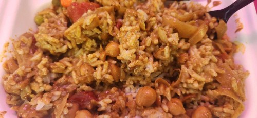 A close-up of a mixed rice dish with vegetables and chickpeas, served in a white container.