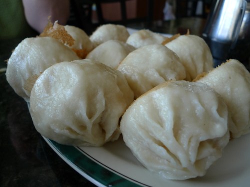 A plate of soft, steamed dumplings with a slightly wrinkled surface, arranged neatly.