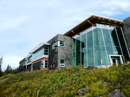 Modern building with large glass windows, set against a backdrop of greenery and blue sky.