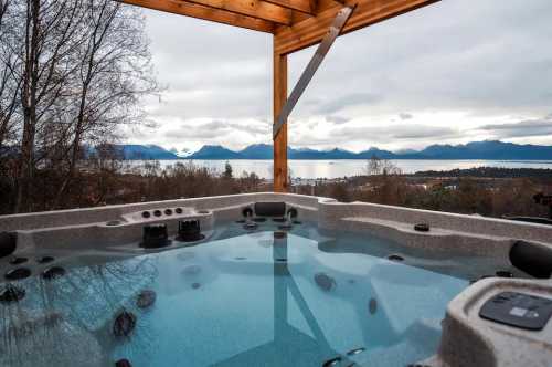 A hot tub with a scenic view of mountains and a lake under a cloudy sky.