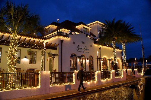 A beautifully lit restaurant with palm trees at dusk, featuring festive lights and a welcoming atmosphere.