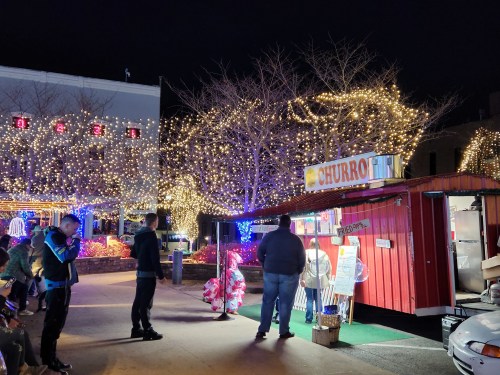 A vibrant night scene featuring a churro stand surrounded by festive lights and people enjoying the atmosphere.