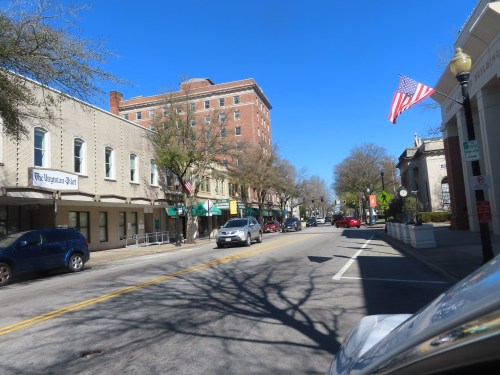 A sunny street view of a small town with buildings, trees, and an American flag waving in the breeze.