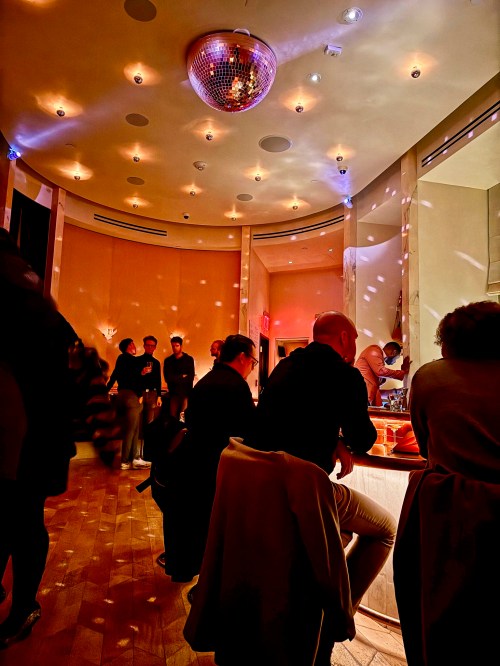 A dimly lit bar scene with a disco ball, patrons seated at the counter, and soft lighting creating a lively atmosphere.