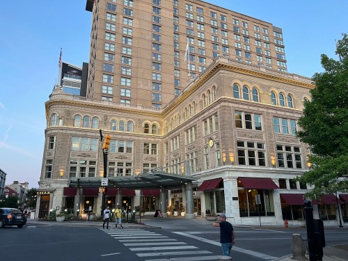 Historic building with modern hotel above, featuring large windows and awnings, at a city intersection during sunset.
