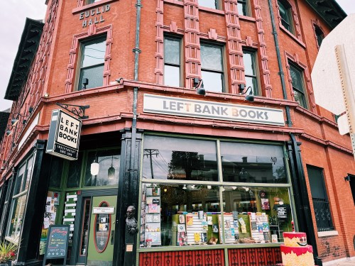 A red brick building with a sign reading "Left Bank Books," featuring large windows and colorful displays.