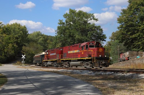 A red and yellow train engine travels along a curved track surrounded by trees and a clear blue sky.