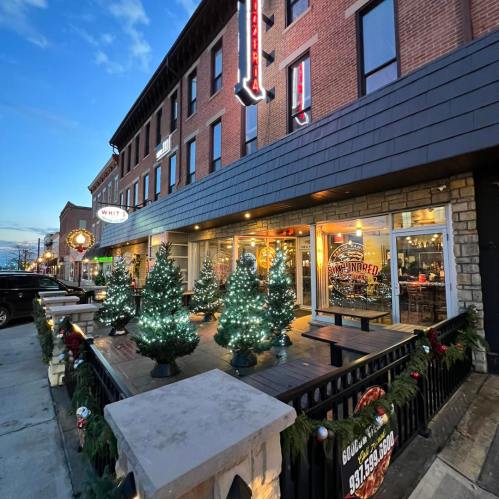 A festive street scene featuring a restaurant with Christmas trees adorned with lights on a decorated patio.