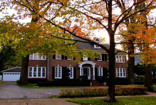 A large brick house surrounded by colorful autumn trees and a well-maintained yard.