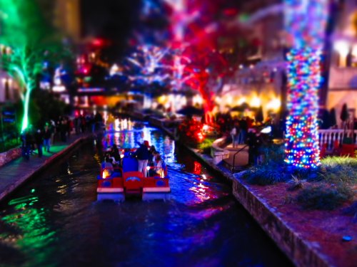 A colorful canal scene at night, with festive lights reflecting on the water and people enjoying a boat ride.