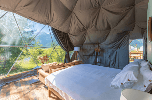 Cozy interior of a geodesic dome with a large bed and scenic views of nature through large windows.