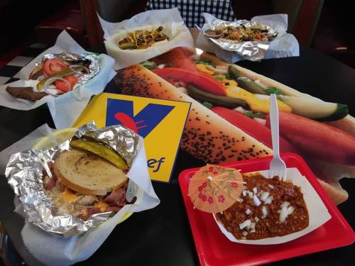 A table with various dishes: sandwiches, chili, and hot dogs, all served in colorful wrappers and plates.