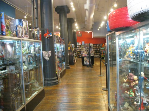 A spacious store aisle lined with display cases of collectibles and shelves filled with books and merchandise.