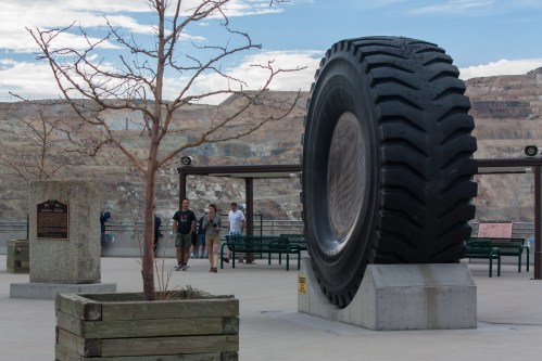 A large tire sculpture stands in an outdoor area with visitors and a barren tree in the background.