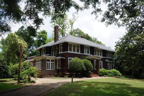 A large, two-story house with a dark roof, surrounded by greenery and trees on a sunny day.