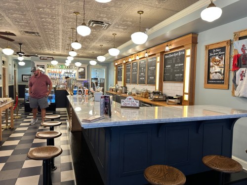 A cozy diner interior with a marble counter, stools, and a menu board, featuring a customer browsing the space.