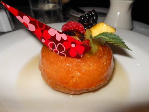 A round dessert topped with colorful fruit and a decorative red paper, served on a white plate.