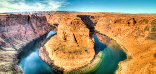 Aerial view of Horseshoe Bend, showcasing a winding river surrounded by towering red rock formations under a clear blue sky.