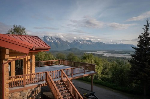 A scenic view from a wooden deck overlooking mountains and a river under a clear sky.