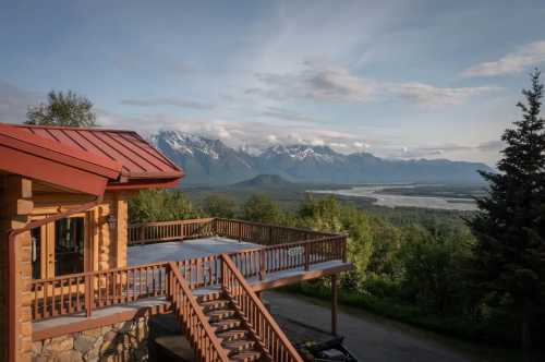 A scenic view from a wooden deck overlooking mountains and a river under a clear sky.