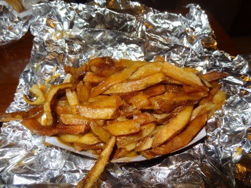 A serving of golden-brown French fries piled on a piece of foil.