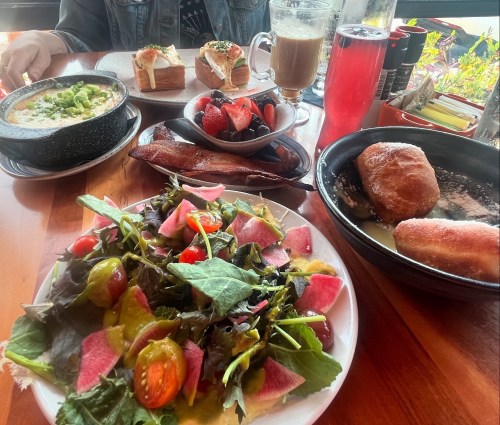 A table set with a colorful salad, baked goods, a creamy dish, and drinks, showcasing a delicious brunch spread.