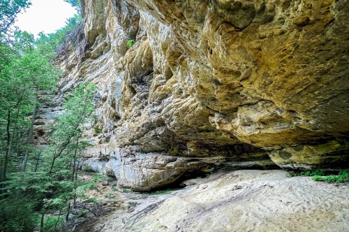 The soft sand under a massive limestone wall filled with holes and hues of colors.