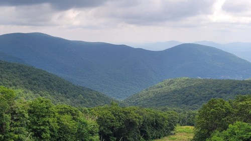 Lush green mountains stretch under a cloudy sky, creating a serene landscape of rolling hills and valleys.