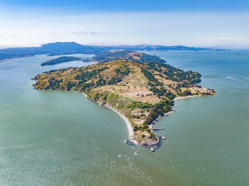 Aerial view of a lush green island surrounded by water, with hills and distant mountains in the background.