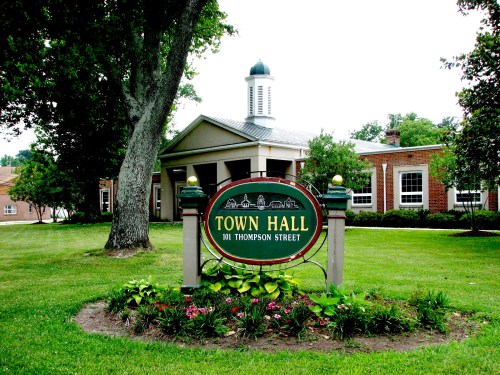 Sign for Town Hall at 101 Thompson Street, surrounded by greenery and flowers, with a building in the background.