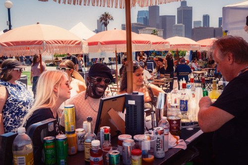 A lively bar scene with people chatting, drinks on the counter, and a city skyline in the background.