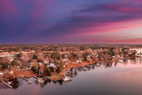 Aerial view of a serene lakeside community at sunset, with colorful skies and boats docked along the shore.