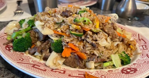 A heaping pile of beef fried rice on a glass plate with red trim.