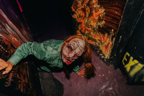 A creepy figure with a grotesque face and long hair crawls in a dark, eerie hallway with colorful splatters on the walls.