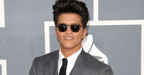 Bruno Mars on the red carpet wearing sunglasses and a grey suit