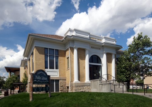 Historic brick library building with large windows, a decorative entrance, and a green lawn under a partly cloudy sky.