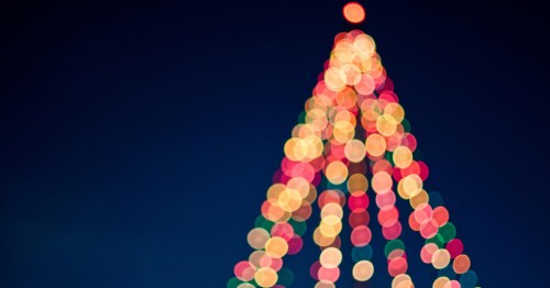 Brightly lit, triangular pattern of colorful Christmas lights, creating a bokeh effect against a deep blue night sky.