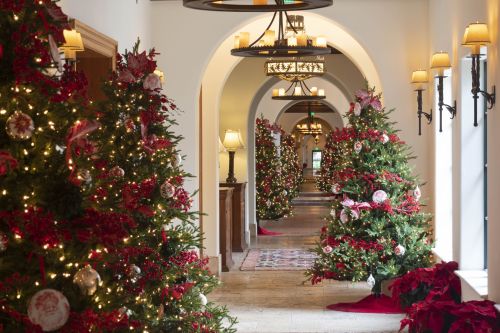 A festive hallway adorned with Christmas trees, red decorations, and warm lighting, creating a cozy holiday atmosphere.